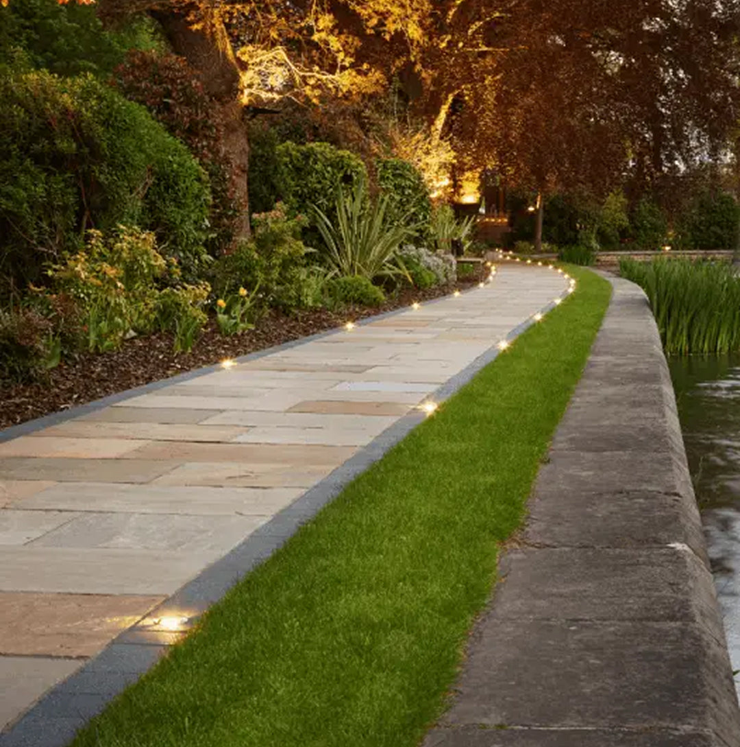 Evening garden pathway with illuminated lights and green grass.
